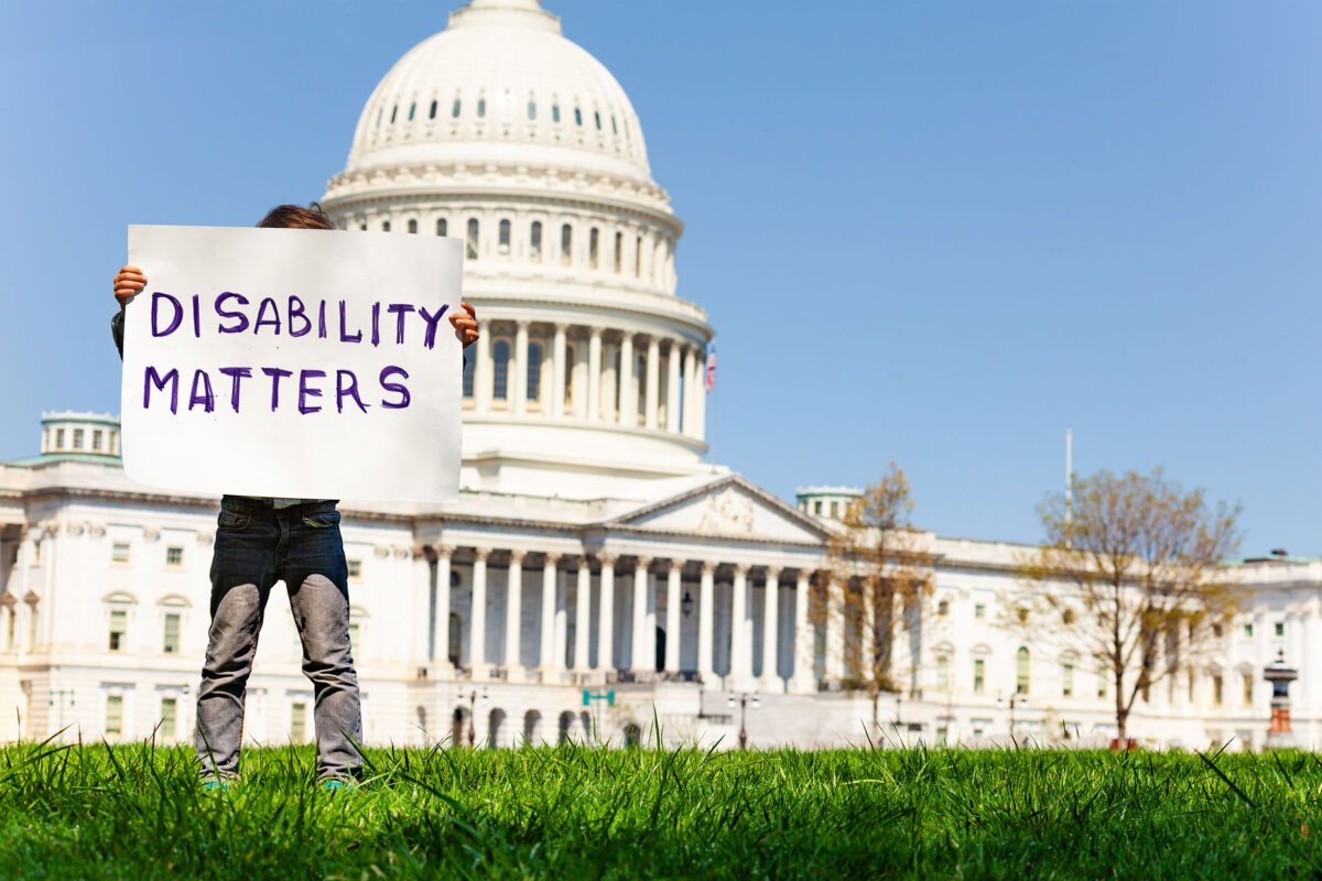 A person holding a sign that reads "Disability Matters" in front of the Capitol building
